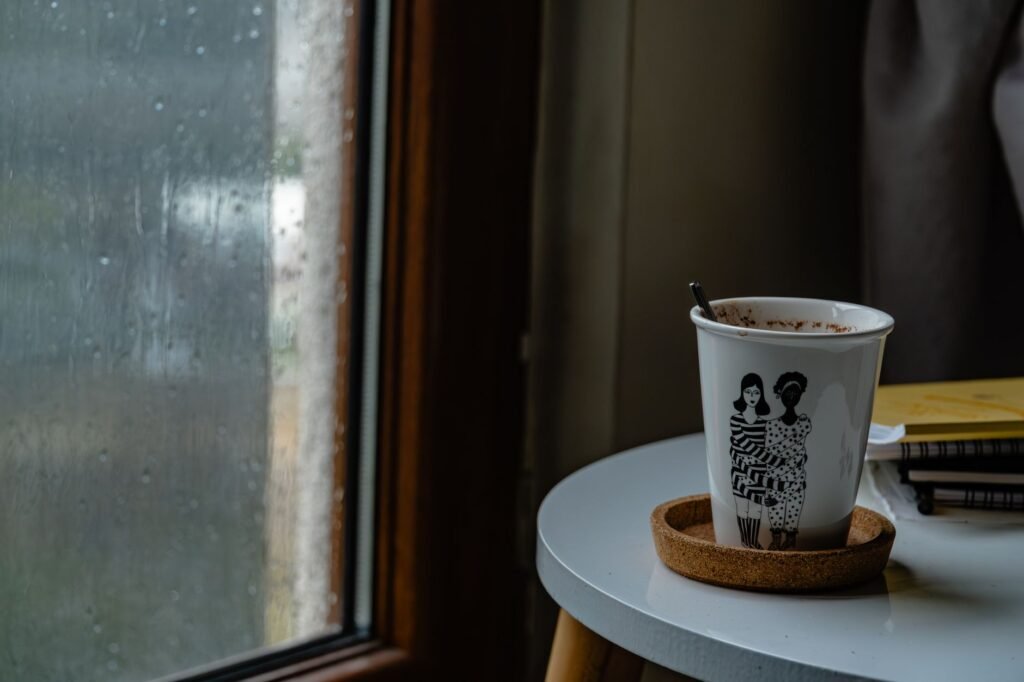 A cozy coffee cup with artistic design sits on a table by a rainy window, creating a serene indoor scene.