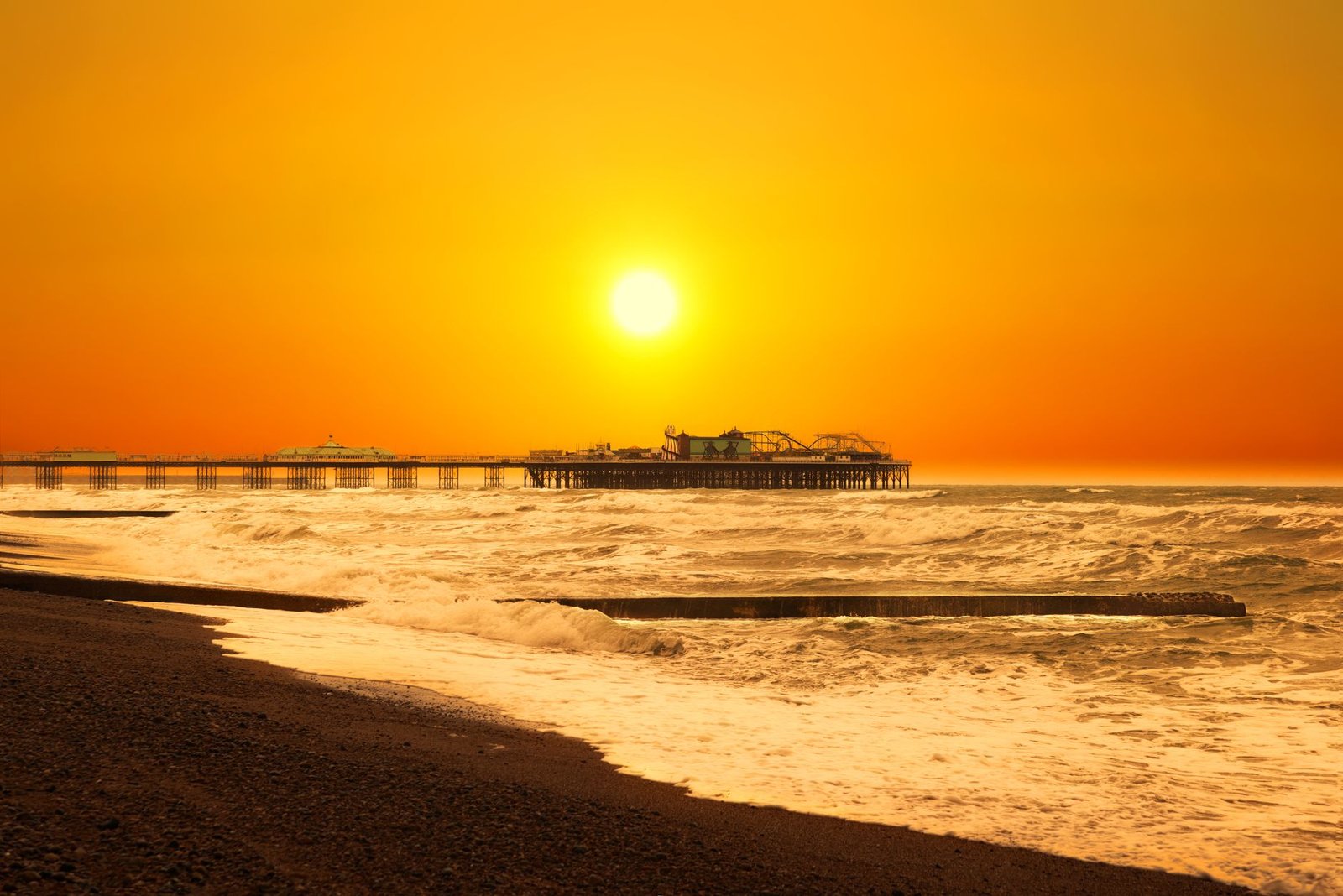 A stunning view of Brighton Pier silhouetted against a golden sunset over the sea waves.