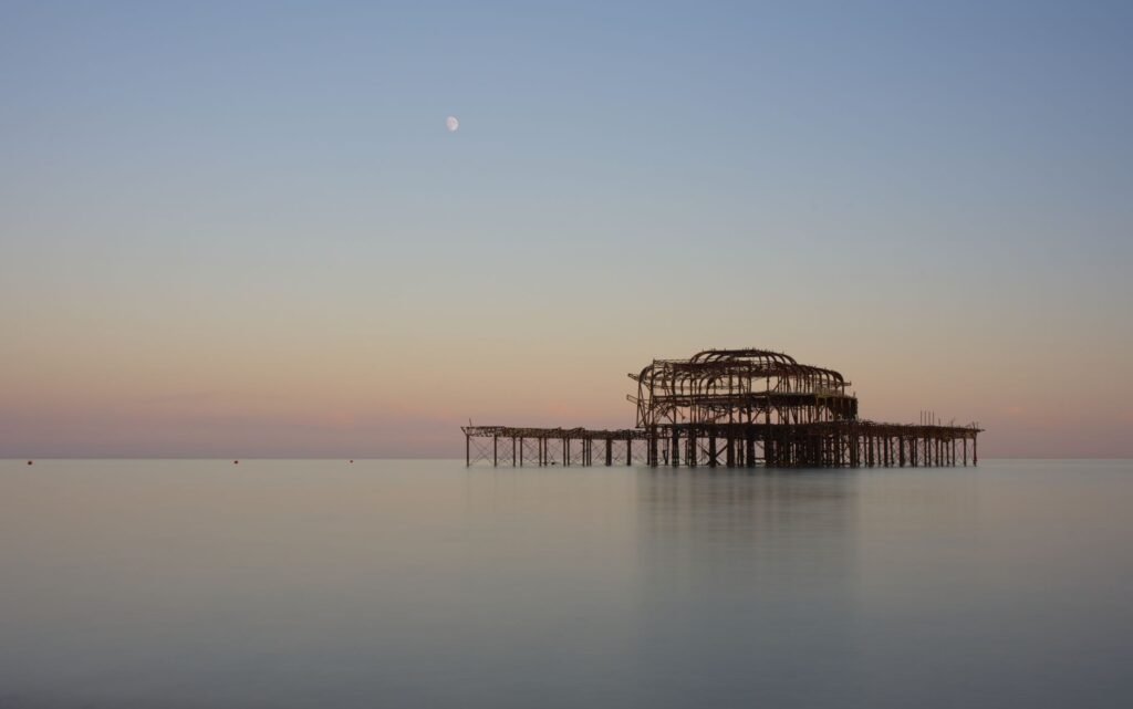 A tranquil scene of Brighton's iconic West Pier at twilight, with soft pastel skies reflecting over calm waters.