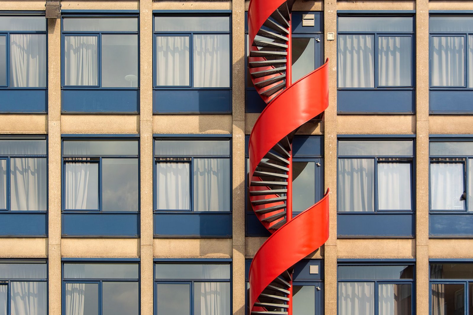 Urban building facade featuring a striking red spiral staircase, adding artistic flair to modern architecture.