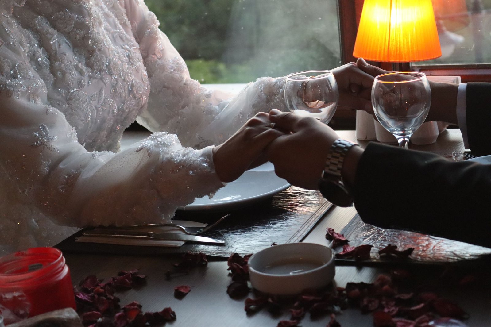 Bride and groom holding hands at a romantic dinner setting with soft lighting.