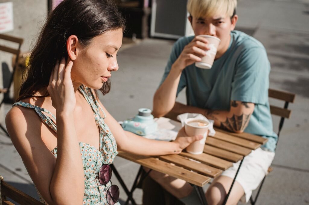 Young tender dreamy girlfriend and Asian pensive boyfriend with cup of hot coffee on sunny street