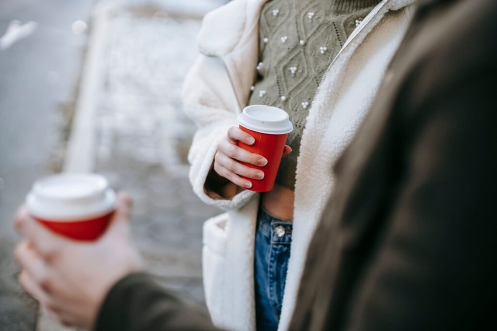 Crop anonymous stylish female in trendy outfit drinking takeaway coffee while standing on city street with boyfriend