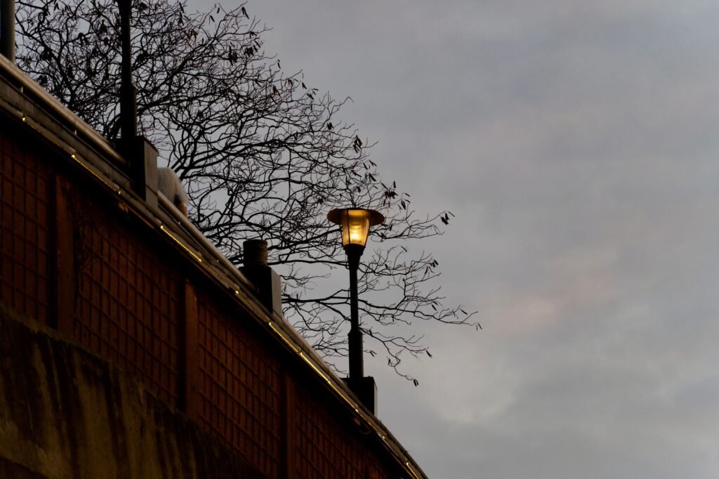 A lone street lamp glows warmly against a moody evening sky near a bridge.
