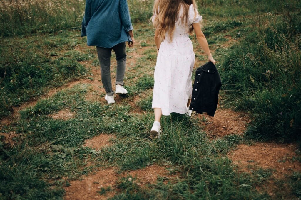 A couple strolls through a lush green meadow in summer, capturing a serene outdoor moment.