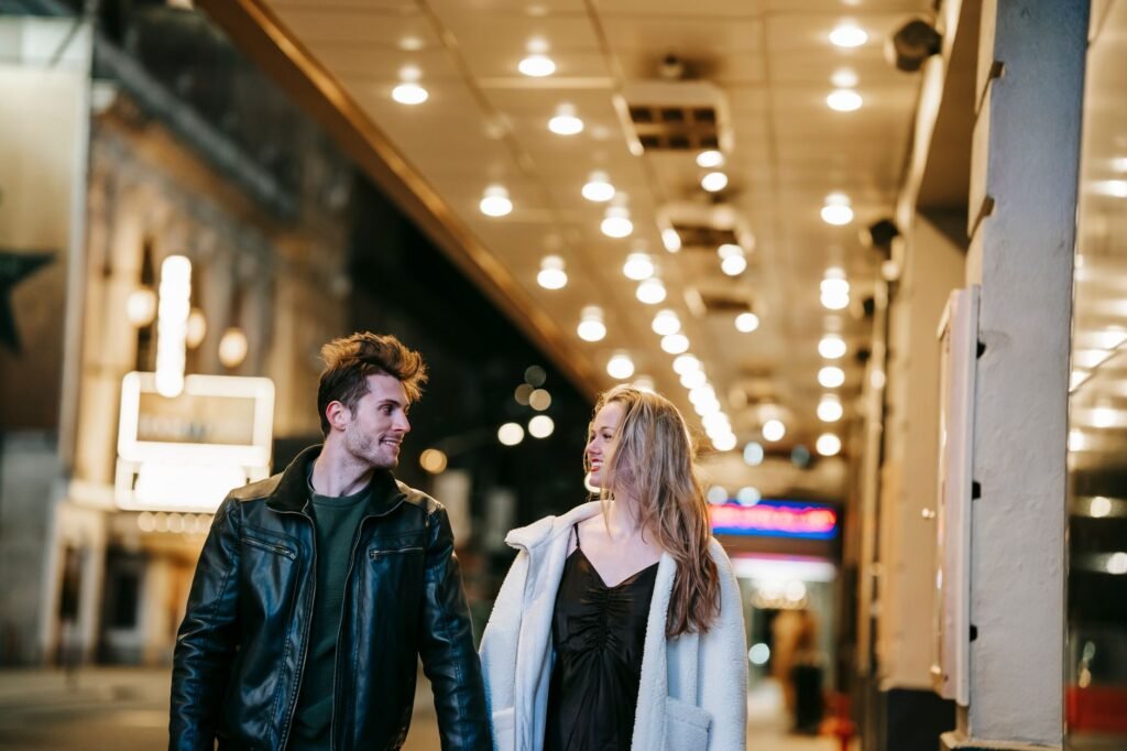 Romantic couple smiling and looking at each other while strolling in hallway of subway station with glowing lights on ceiling