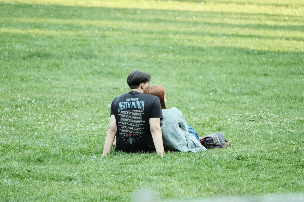 A couple enjoys a peaceful moment together in a sunny park, sitting on the green grass.