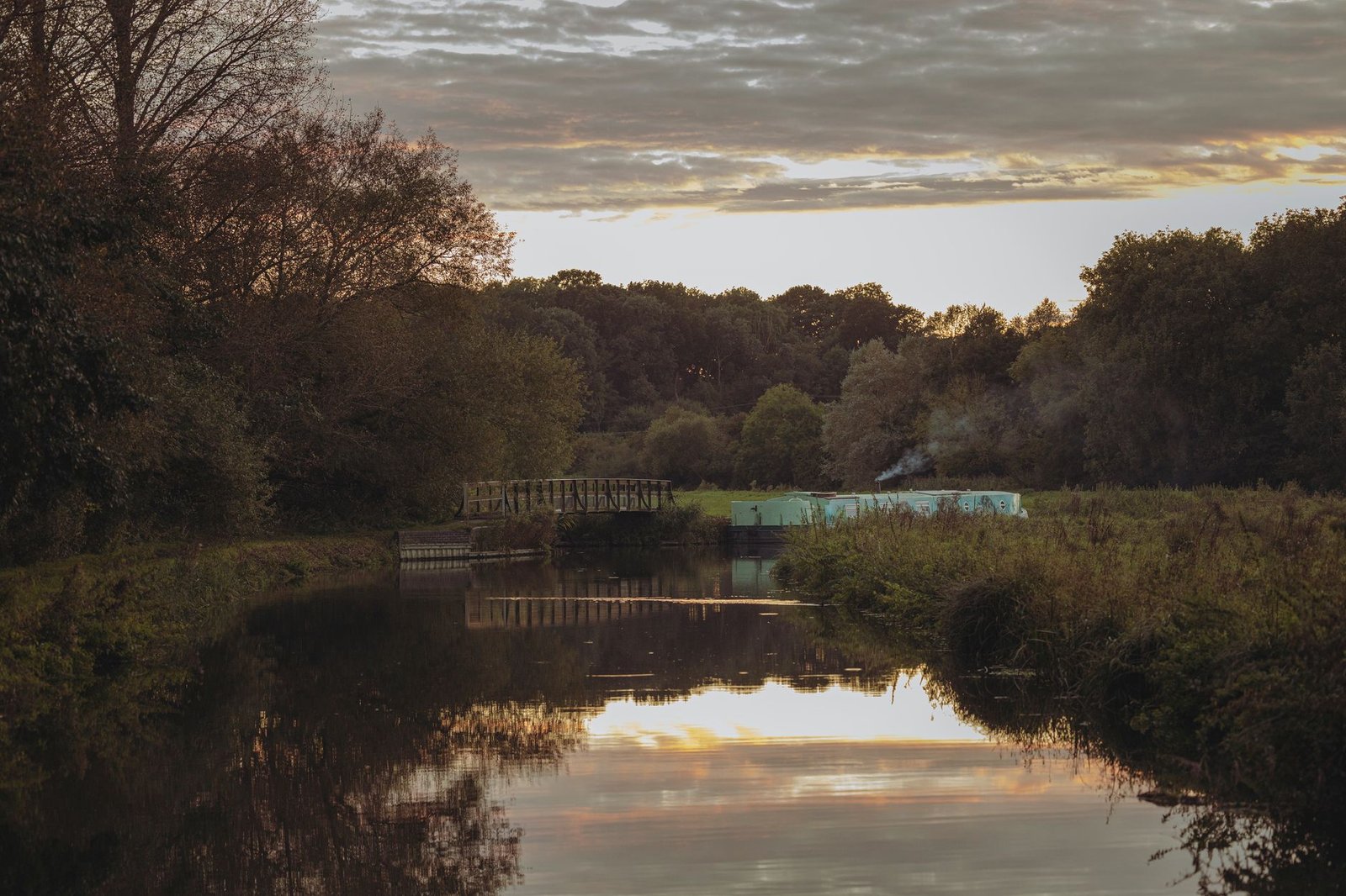 Serene river landscape with bridge and trees at sunset, showcasing natural reflection.