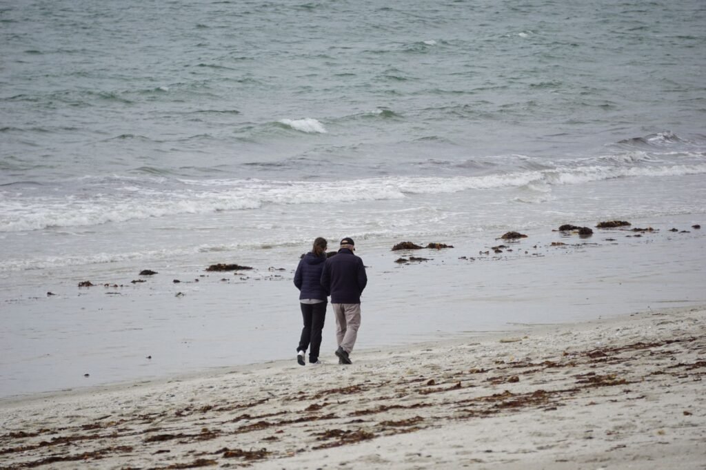 A couple strolling along a serene sandy beach near the ocean during the day.