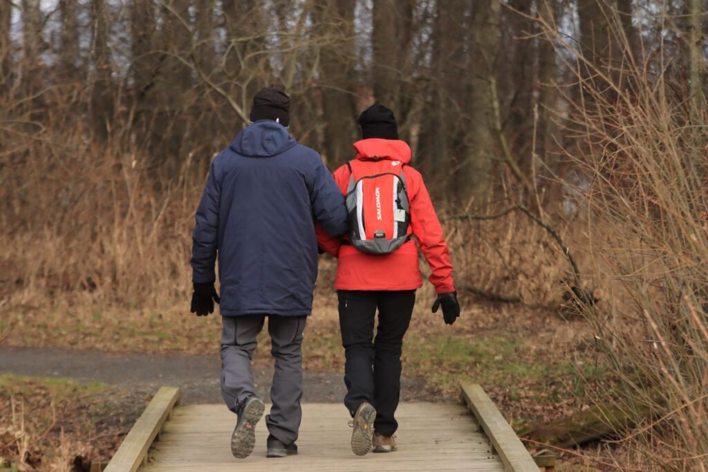 A couple dressed in warm clothing trekking through a forest in winter.