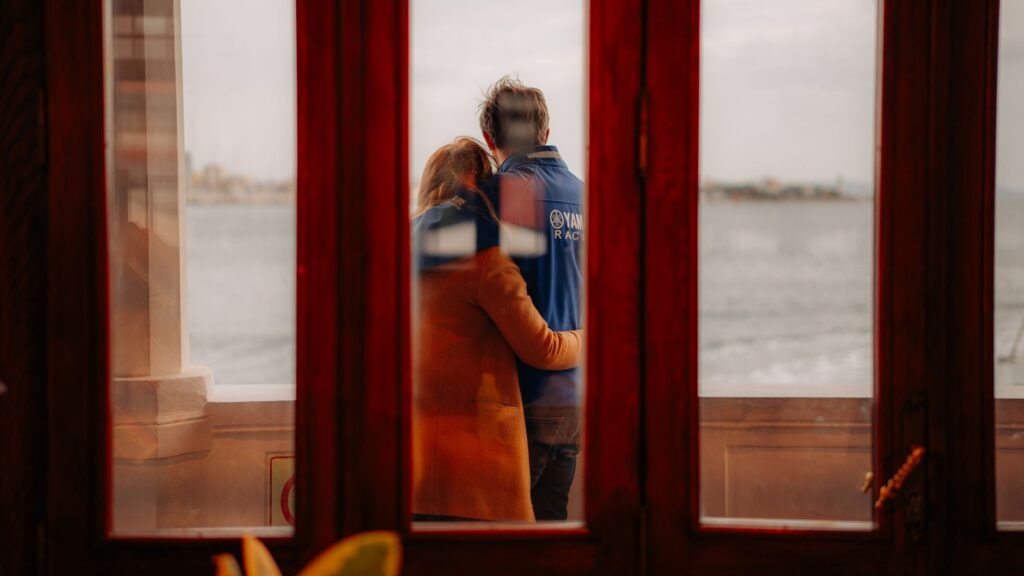 Couple embracing by the sea through a window, exuding warmth and intimacy.