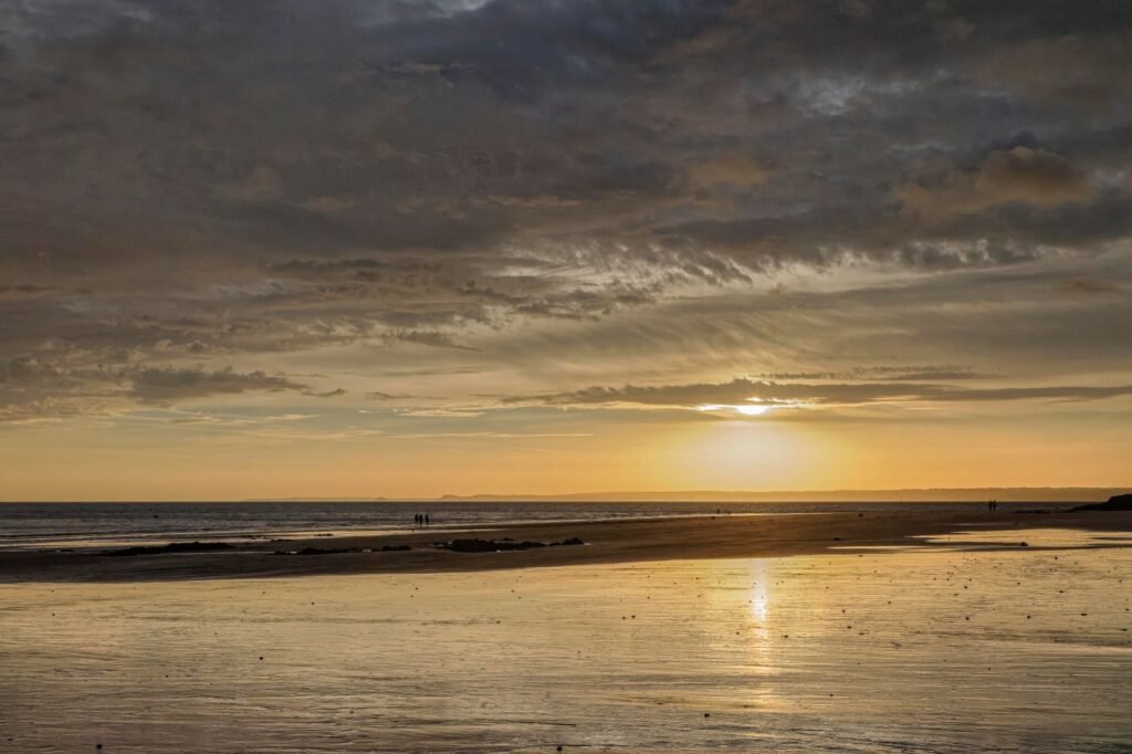 A serene sunset over a Bretagne beach, captured with warm tones and calm waves.