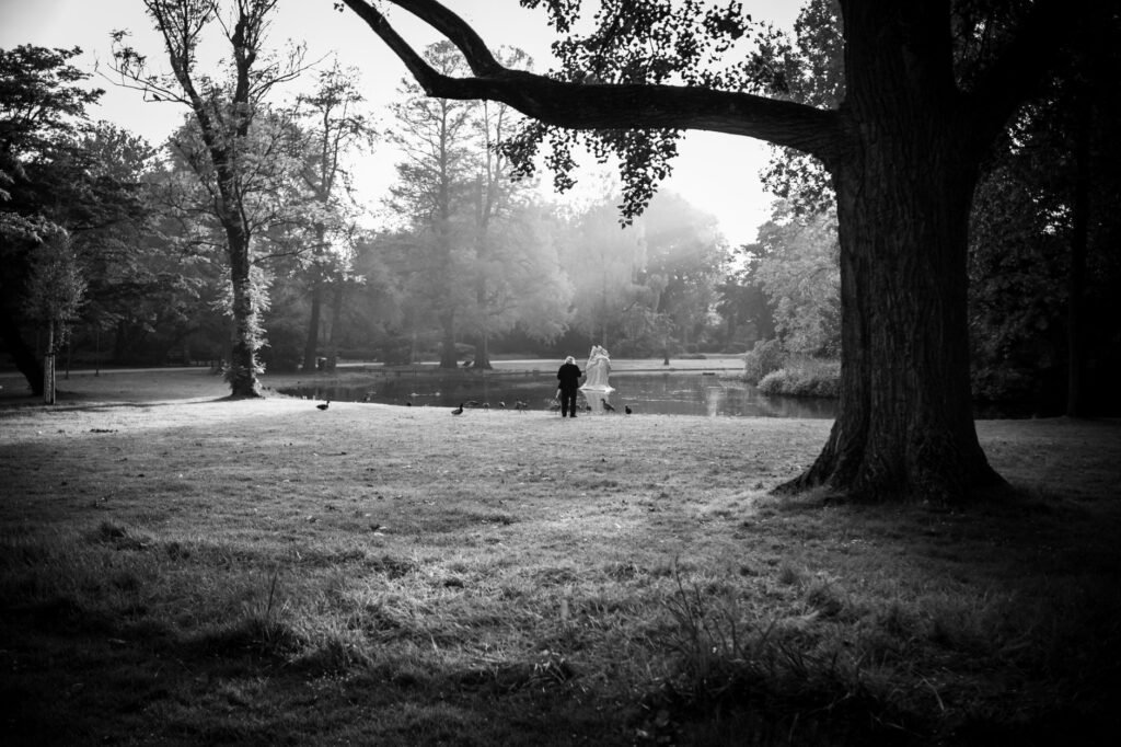 Tranquil black and white scene of two people by a pond in a park, creating a peaceful atmosphere.