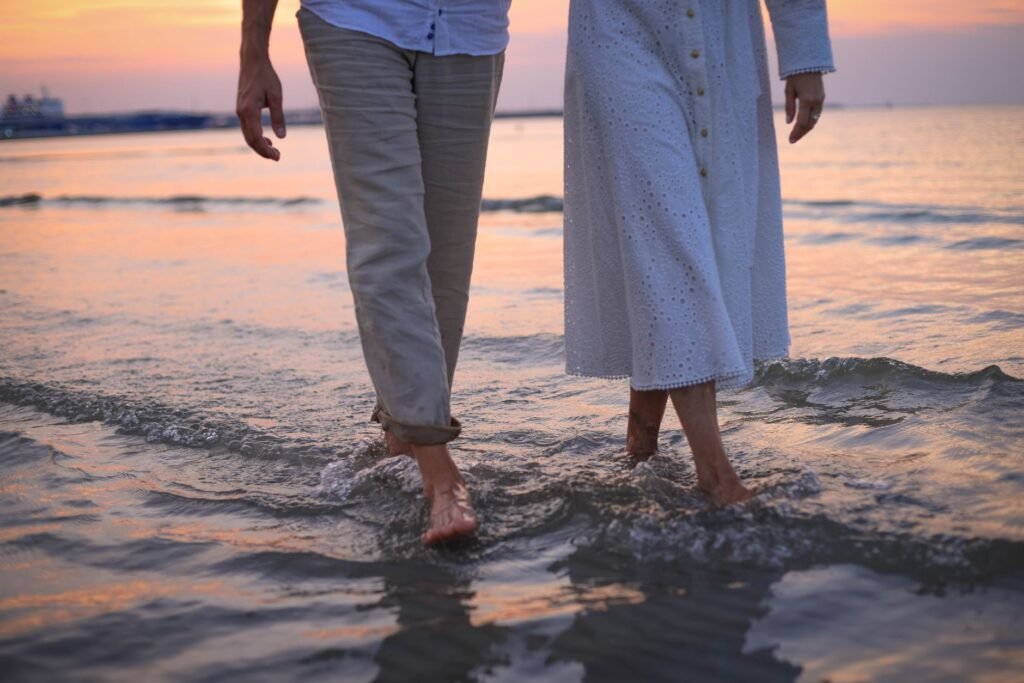 A couple walking barefoot along the beach during sunset, showcasing a romantic and serene scene.