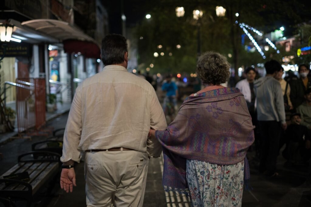 Senior couple walking on a busy nighttime sidewalk, enjoying the evening together.