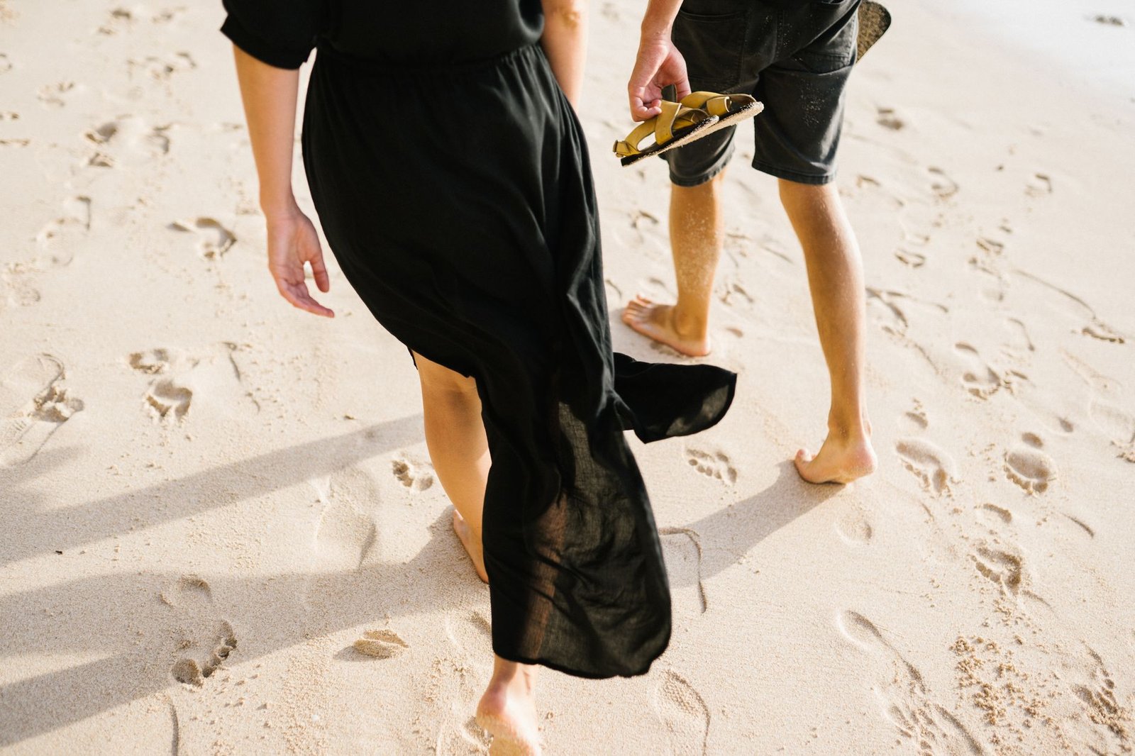 A couple enjoys a romantic barefoot walk on a sandy beach, leaving footprints in the sand.