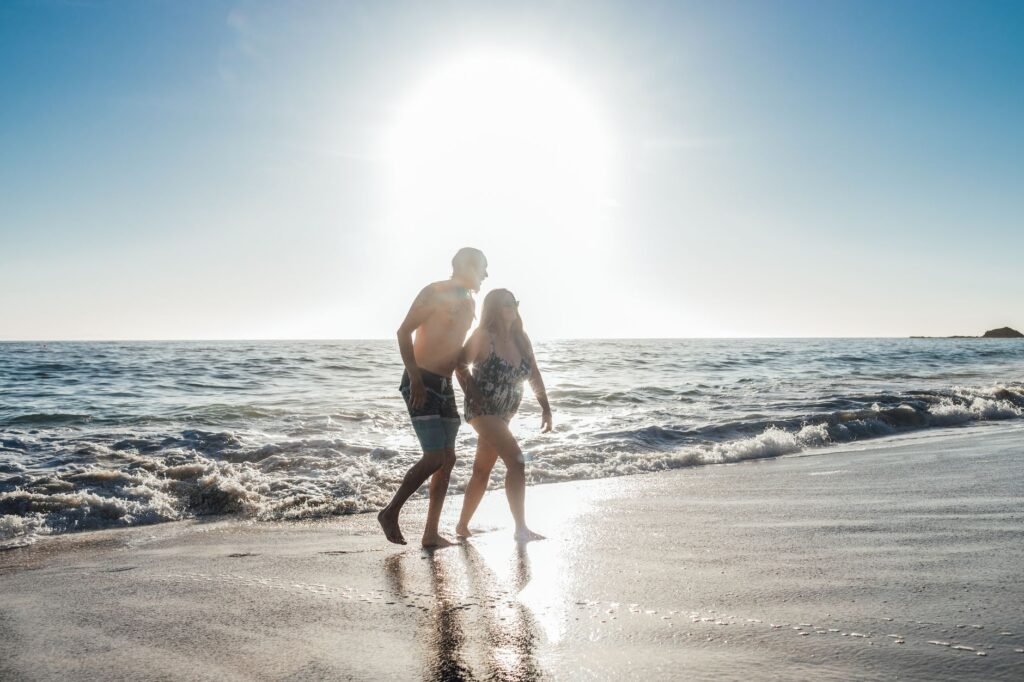 A couple enjoys a romantic walk on a sunny beach with gentle waves.