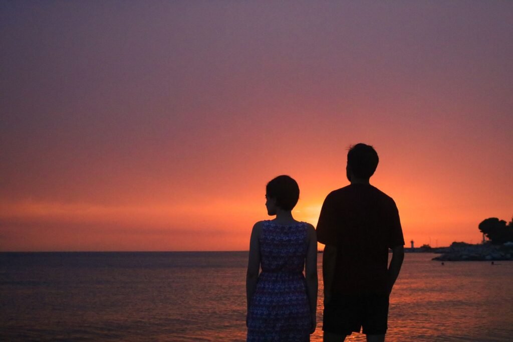 Silhouette of a couple standing by the sea during sunset, creating a serene and romantic ambiance.