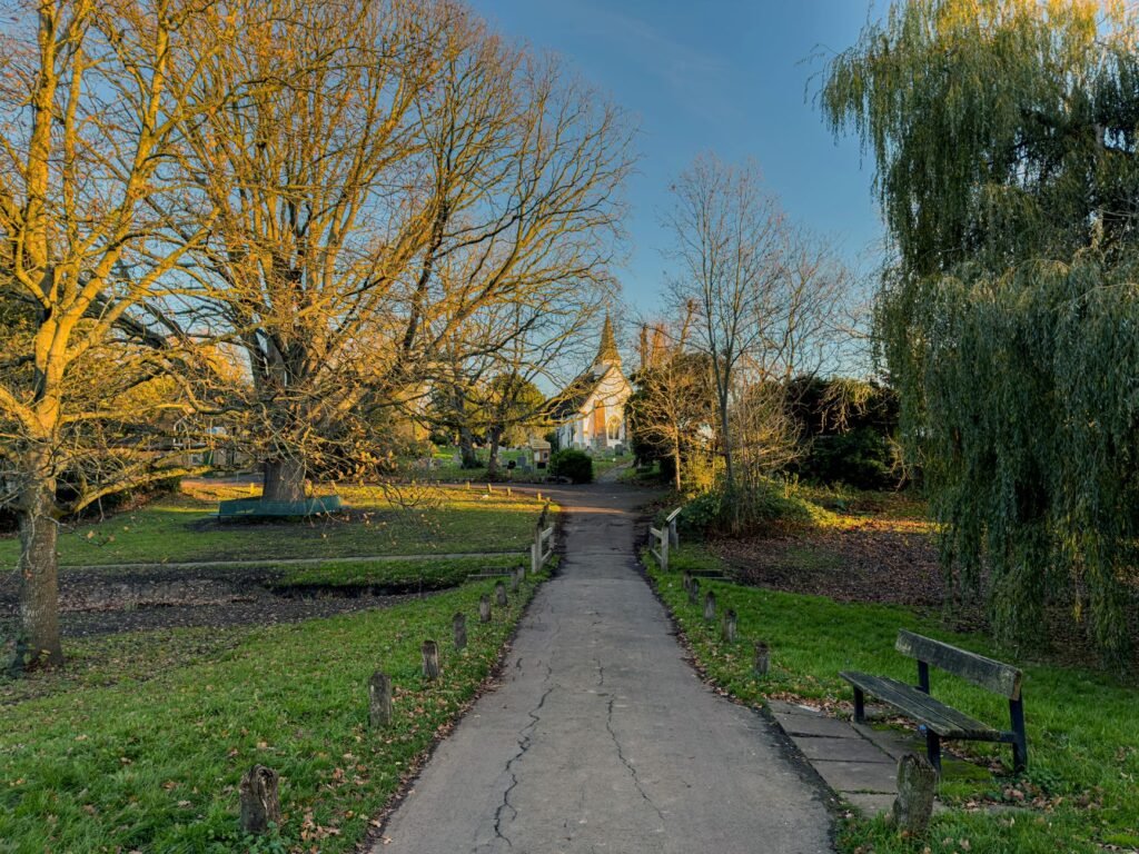 Serene walkway through Greenford Park with church in view, highlighting autumn trees and vibrant twilight sky.
