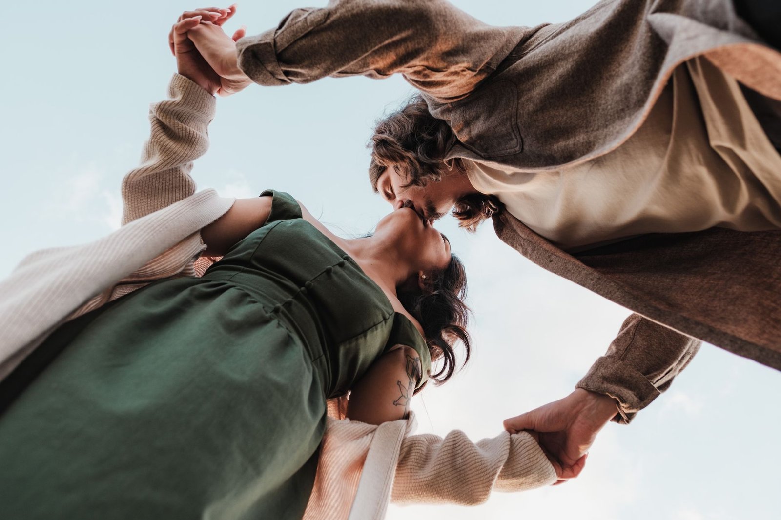 A romantic scene of a couple kissing outdoors, captured from a low angle under a bright blue sky, symbolizing love and connec