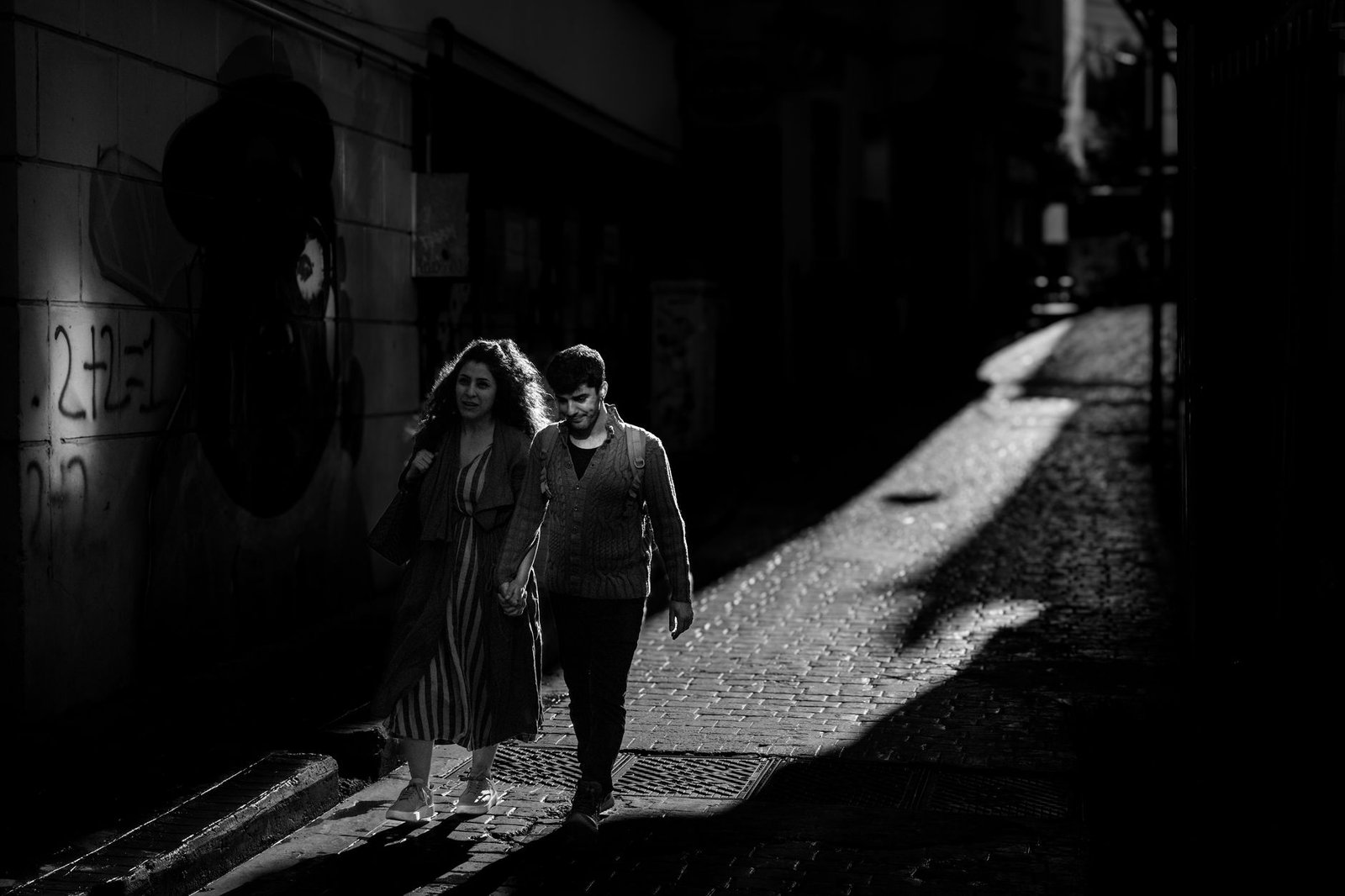 Moody black and white photo of a couple walking in the shadows of Istanbul's streets.