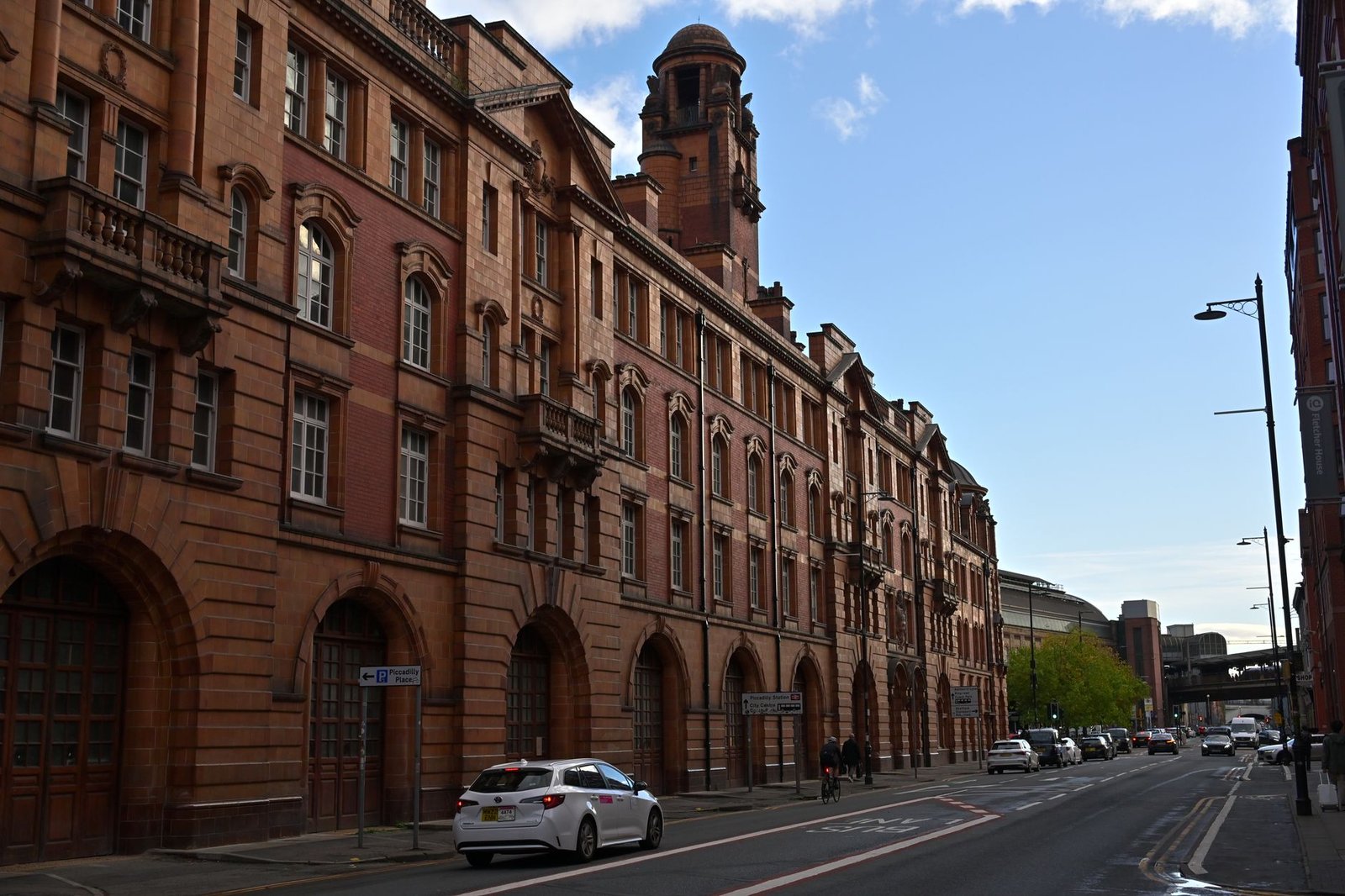 View of a historic red brick building on a street in Manchester on a clear day.