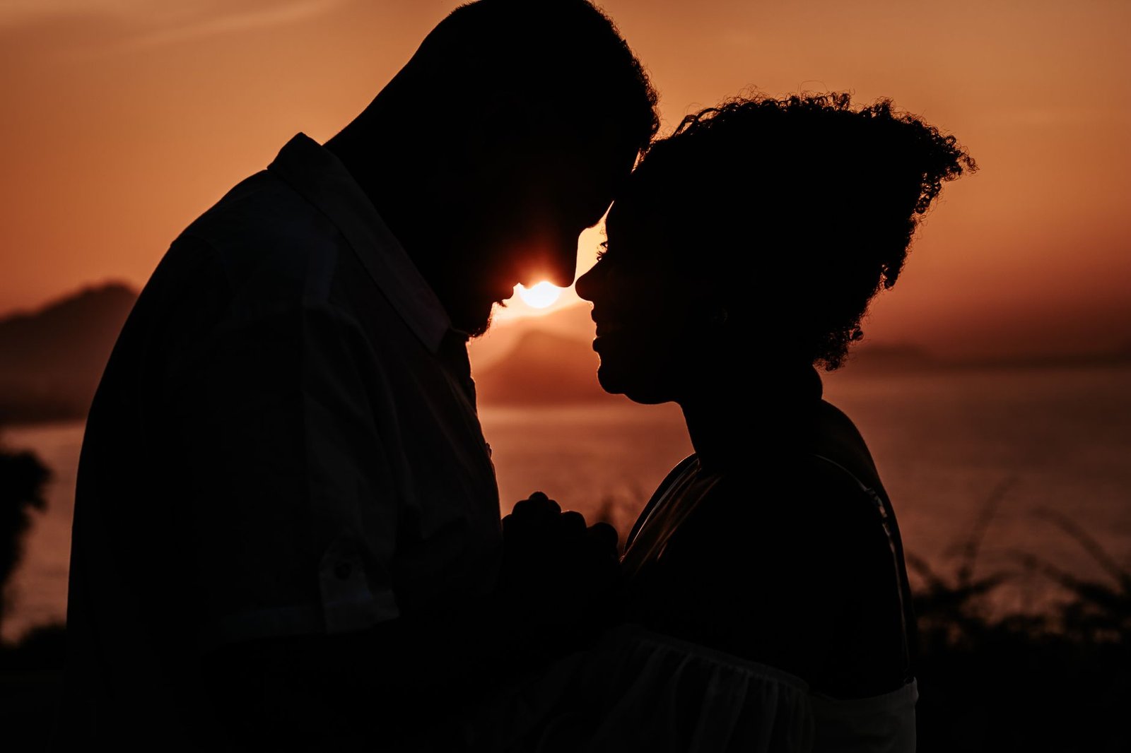 A couple shares an intimate moment in silhouette against a stunning sunset backdrop.