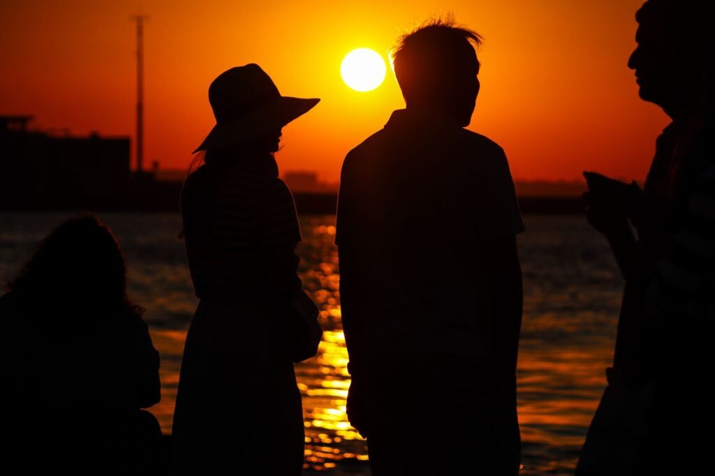 Silhouetted figures enjoy a vibrant sunset by the waterfront, capturing a serene moment.
