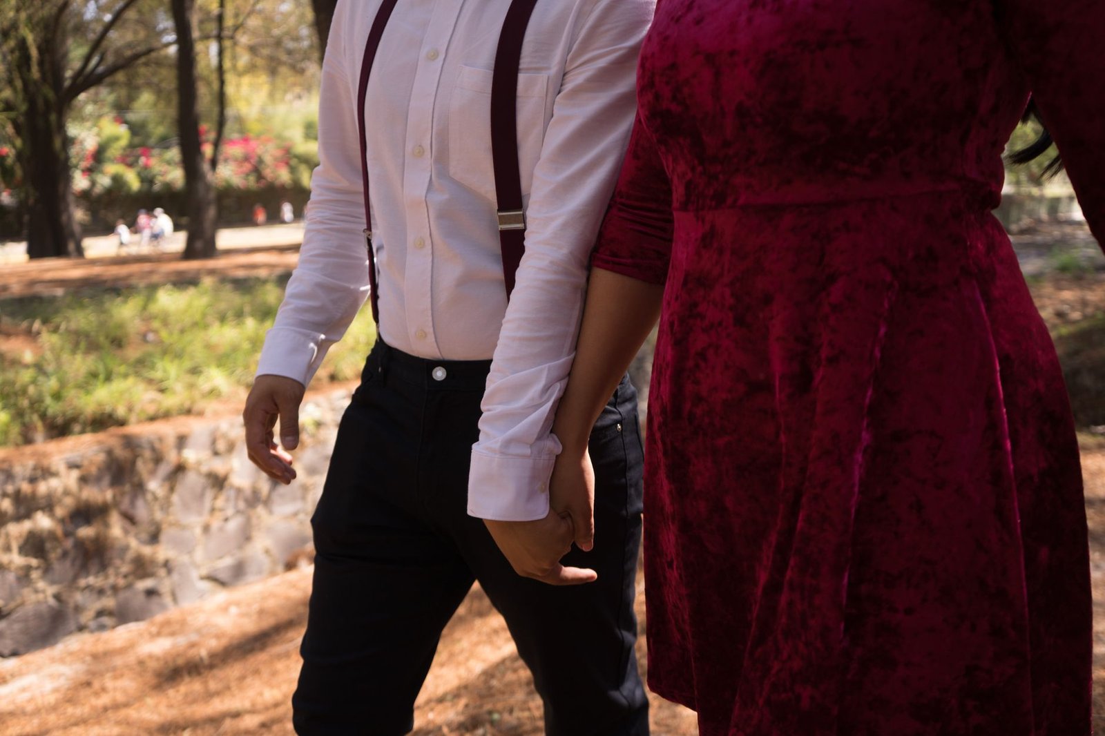 A romantic couple holding hands while walking in a scenic park.