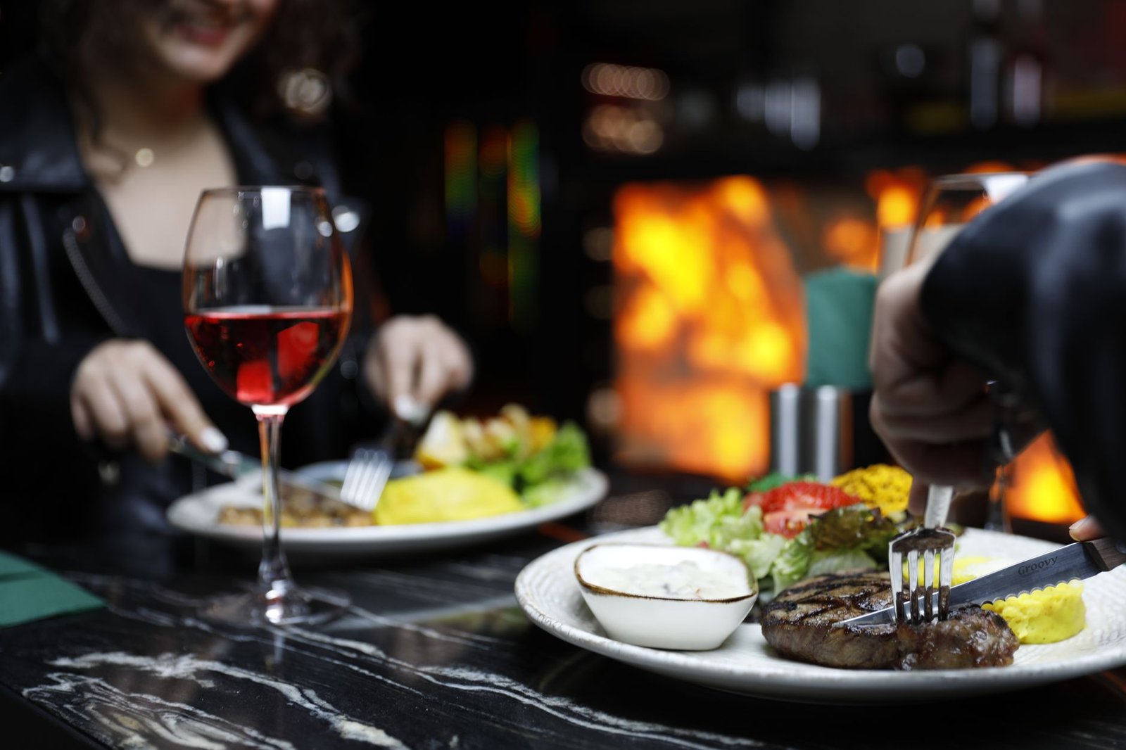 Couple enjoying a cozy dinner with steak and red wine in a warm, intimate setting.