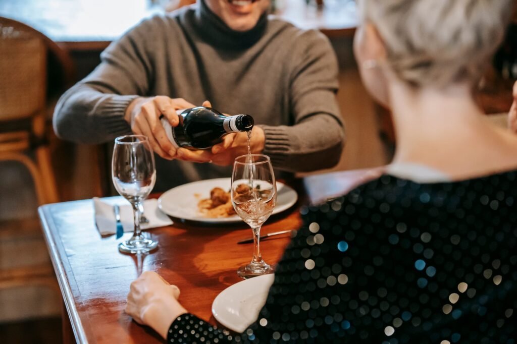 Crop unrecognizable couple having dinner in light room while male pouring wine in glasses at table with plate with pasta with