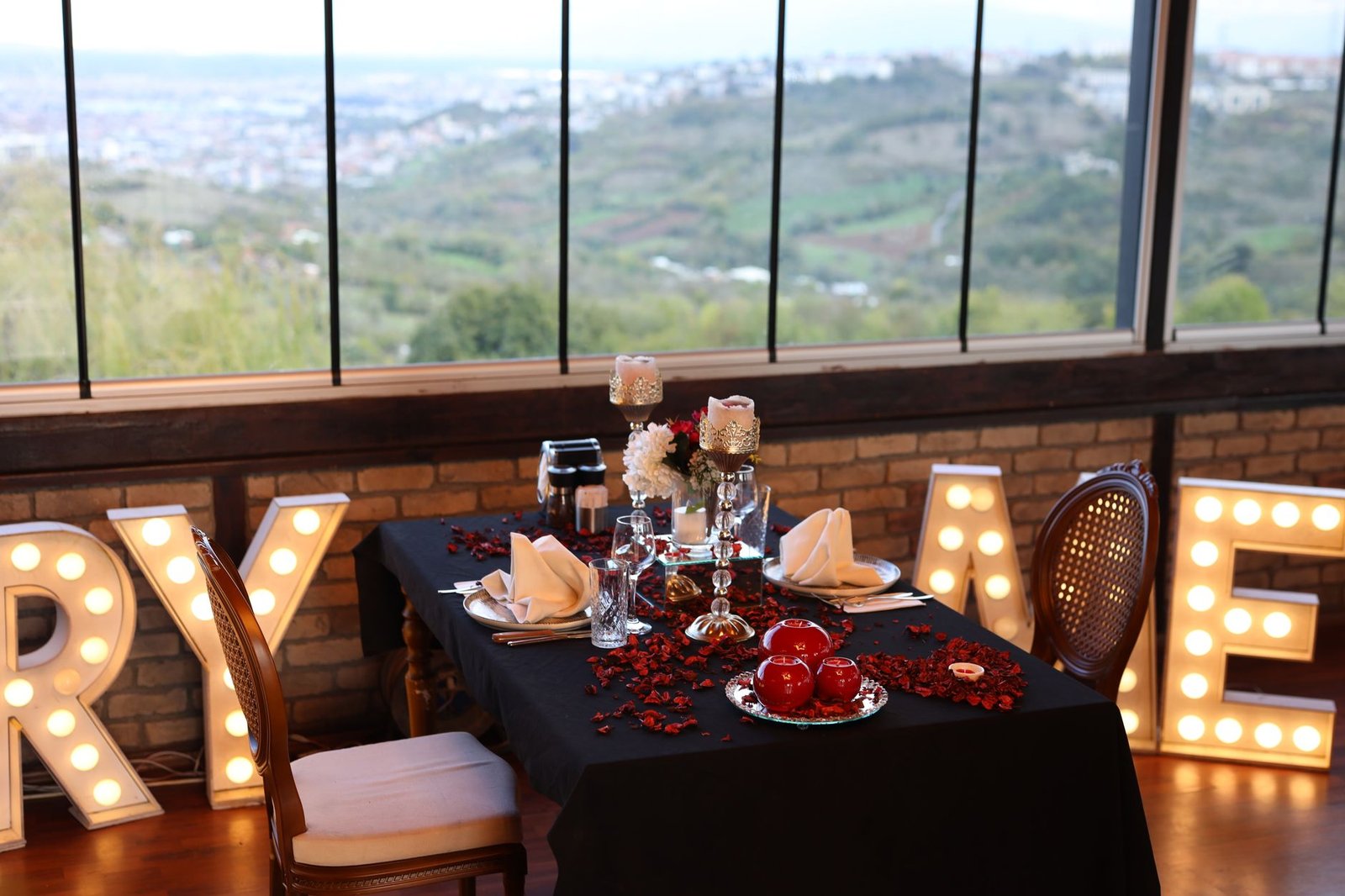 Elegant dining table with lit letters and scenic landscape view through windows.