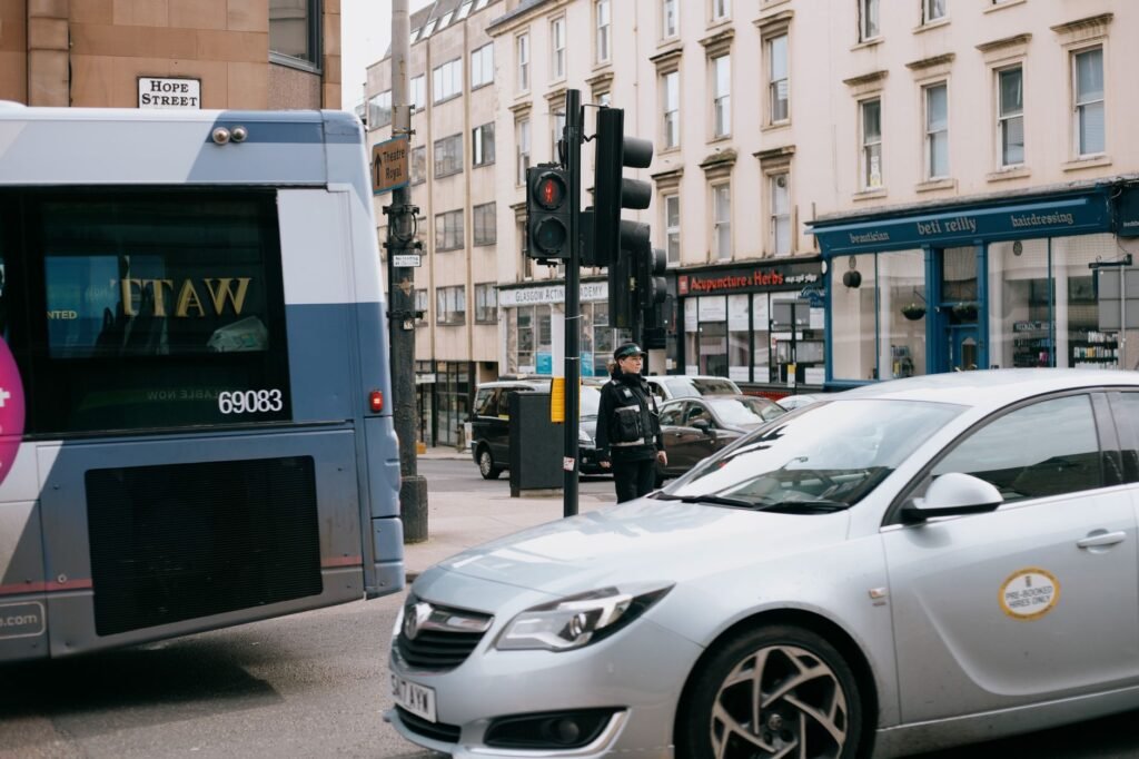 Contemporary bus and automobile on urban roadway near house exteriors and unrecognizable woman in uniform