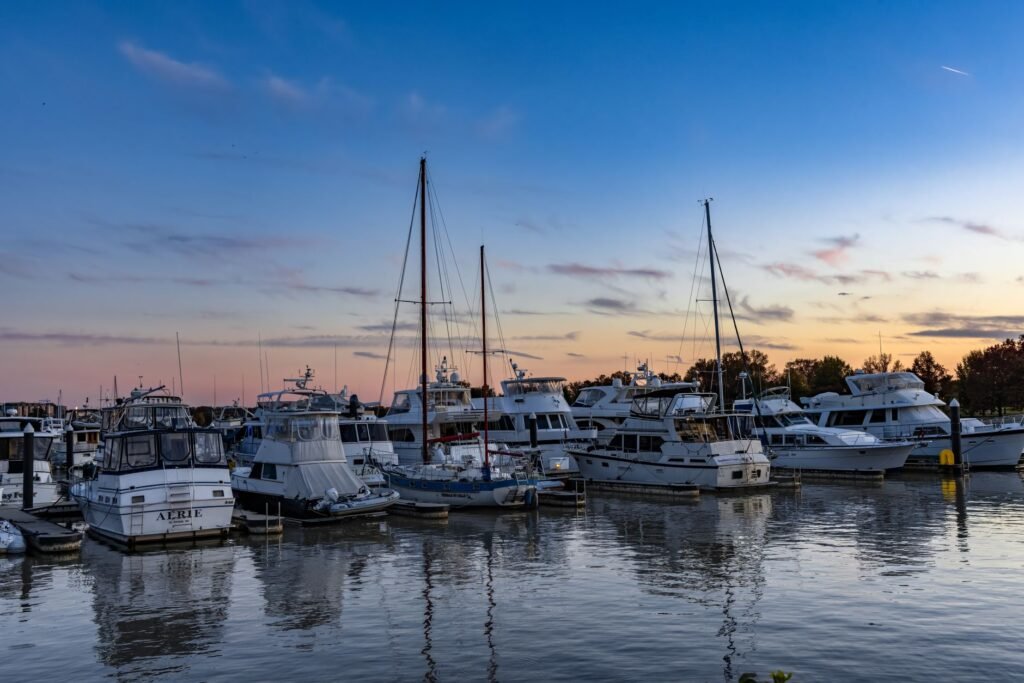 Peaceful marina scene with yachts docked at sunset, reflecting on calm water.