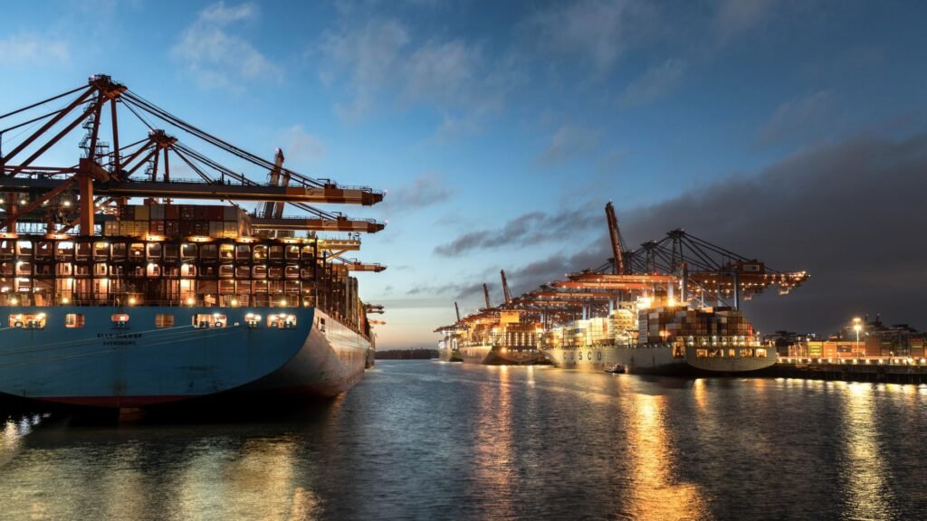Cargo ships docked at Hamburg harbor, illuminated under evening sky. A hub of logistics and commerce.