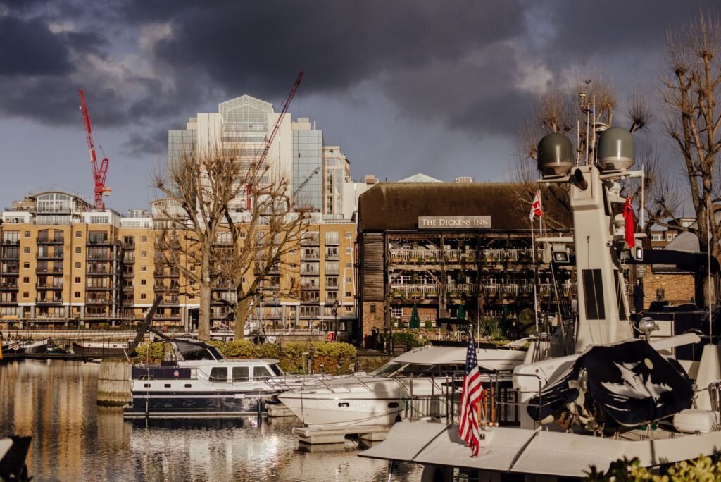 Modern vessels floating near pier with flag on calm river Thames near residential buildings and famous pub in London against