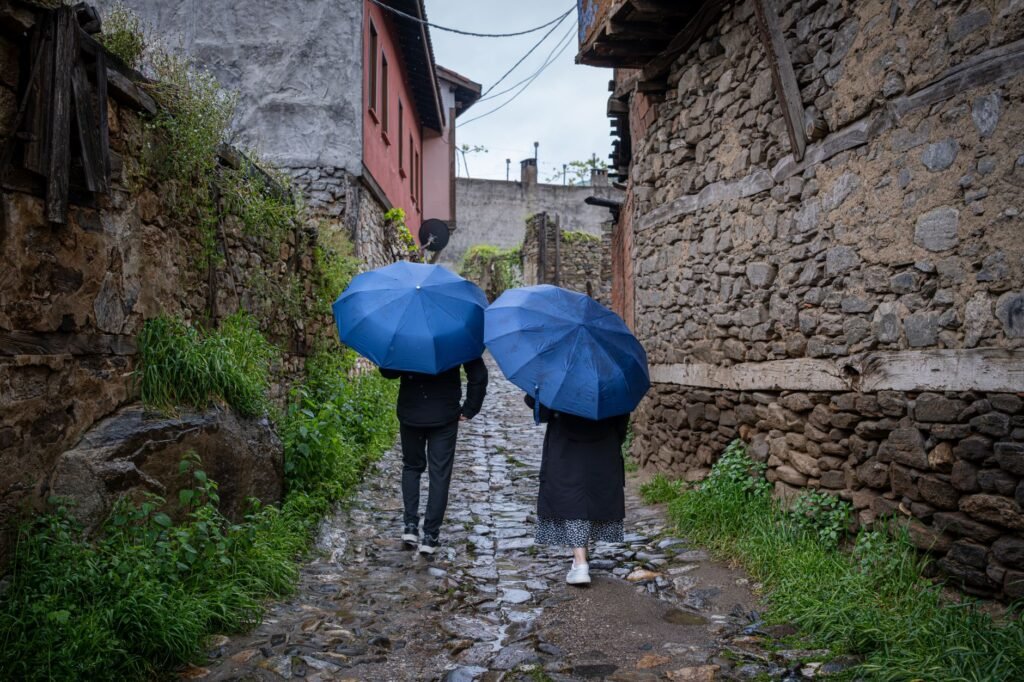 A couple with blue umbrellas strolls down a historic stone alleyway, surrounded by aged architecture.