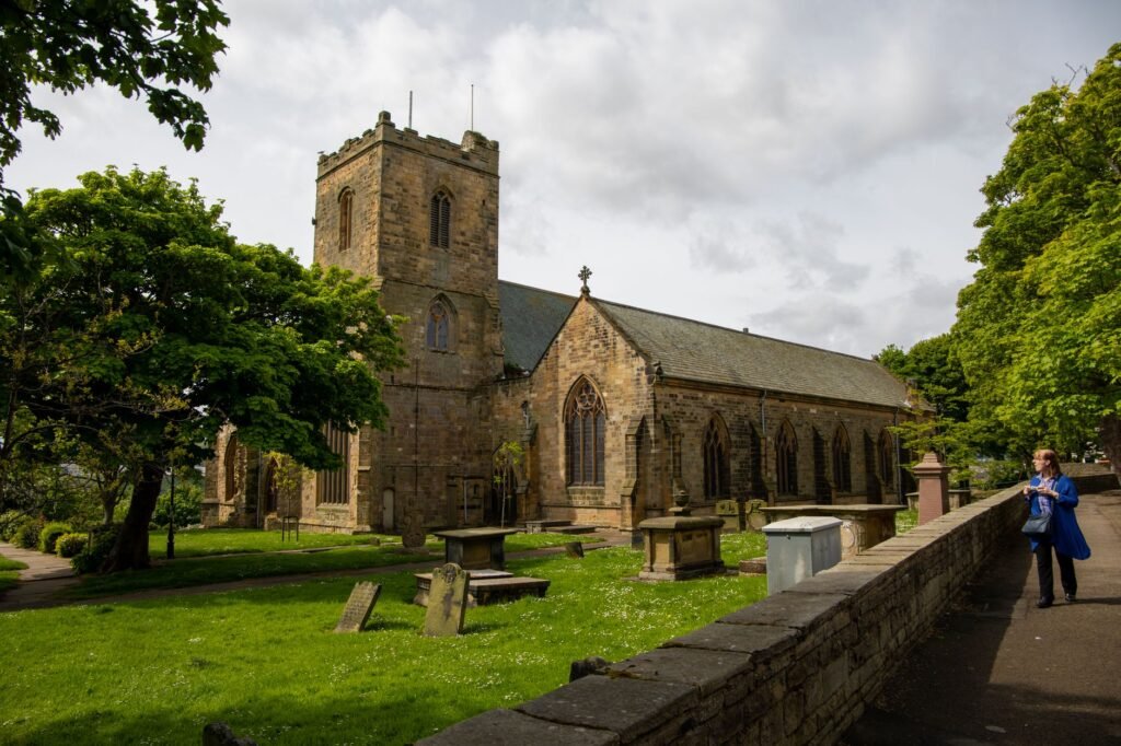 Scenic view of a historic stone church surrounded by green trees and graveyard, capturing a moment of solitude.