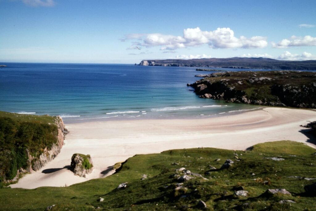 A stunning view of a secluded beach surrounded by cliffs and clear blue waters in Scotland's Highlands.