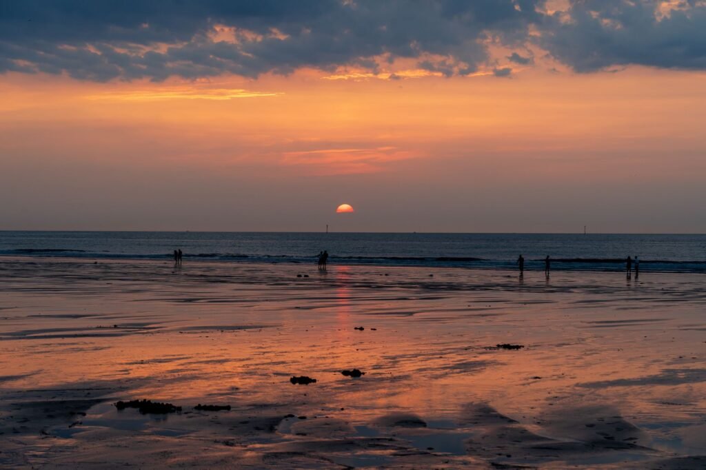 A calming sunset scene with beach reflections and distant silhouettes.