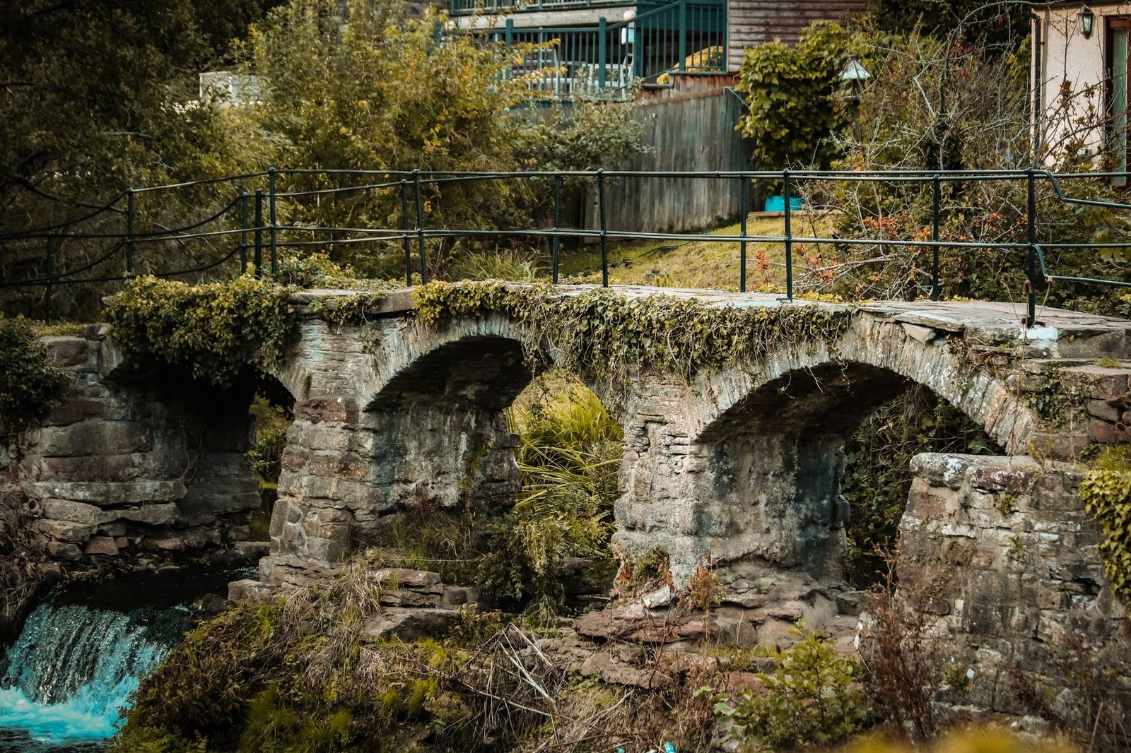 Charming old stone footbridge over a creek in scenic Pensford, surrounded by lush greenery.