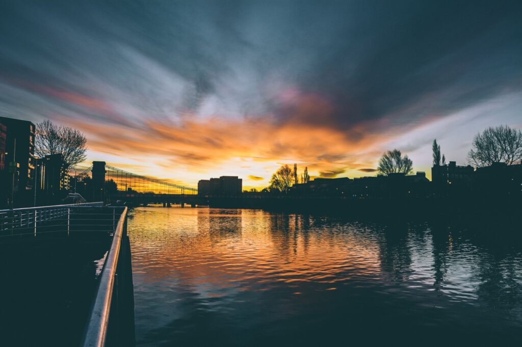Stunning sunset over an urban river with reflective water and silhouetted buildings.