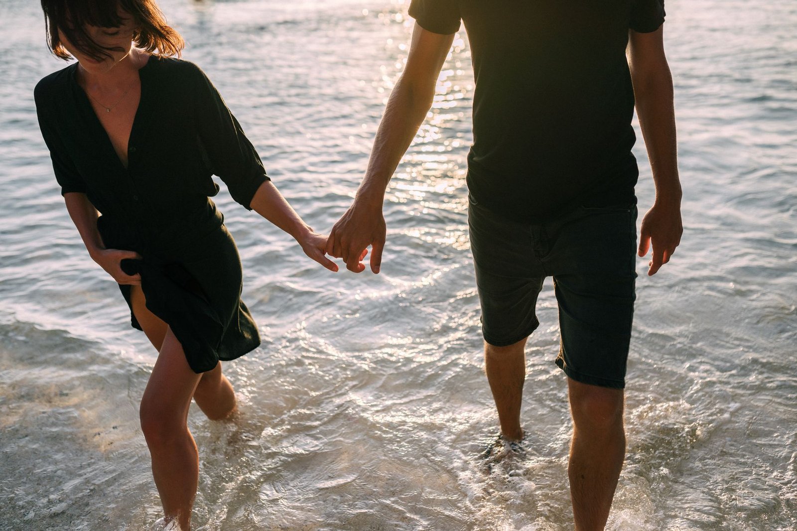 A couple holding hands and walking on the beach at sunset, creating a romantic scene.
