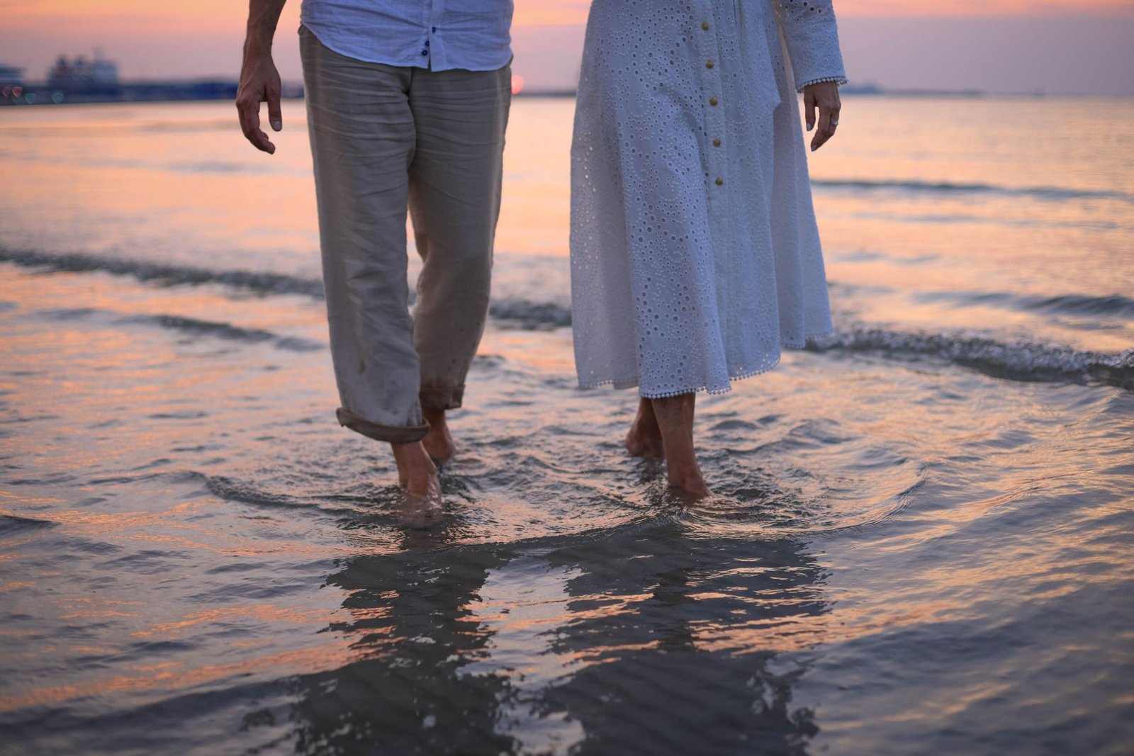 A couple enjoys a barefoot walk along the beach at sunset, creating a romantic atmosphere.