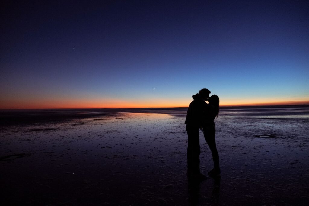 Silhouette of a couple kissing on the beach at sunset, creating a romantic and serene atmosphere.