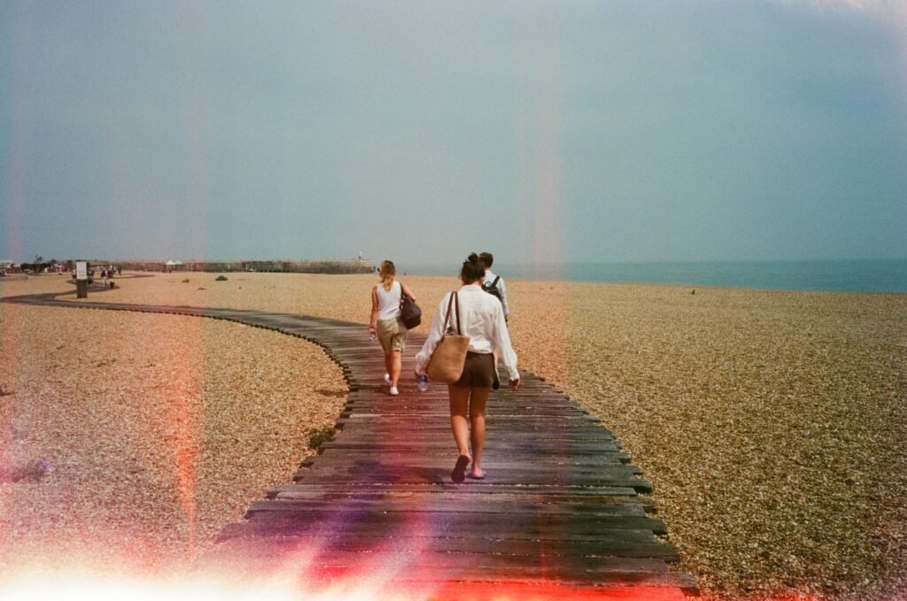 Two people walking along a wooden path on a pebbled beach in Folkestone, capturing a serene coastal scene.