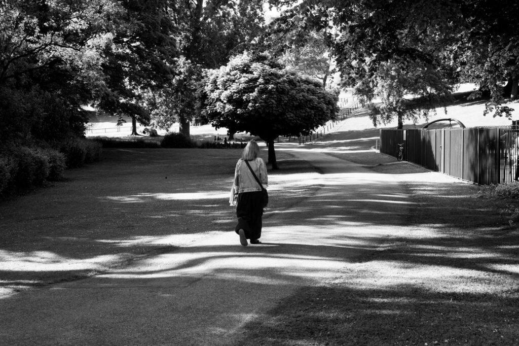 Black and white photo of a person walking in a sunlit park in Dublin, Ireland.