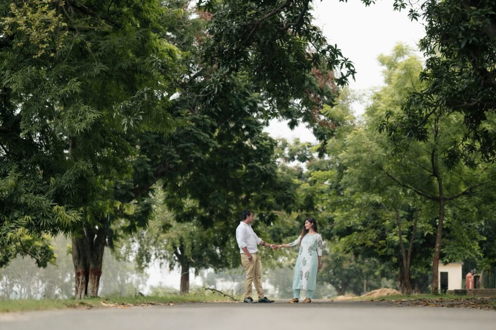 A couple walks hand in hand along a tree-lined path in a lush green park.