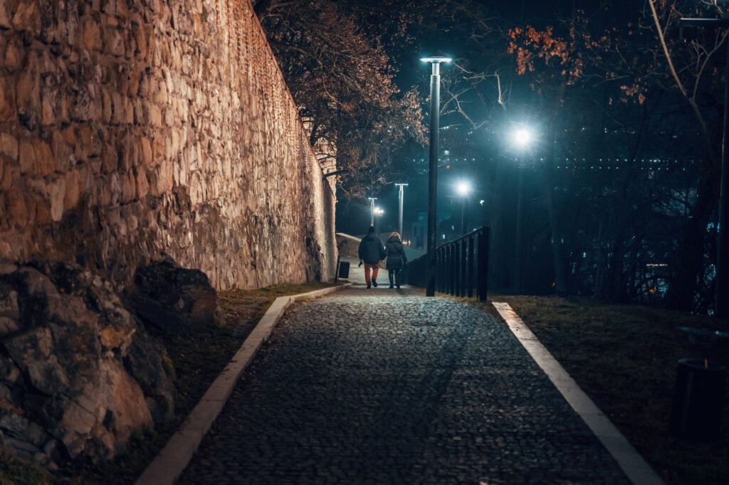 Couple walking down a cobblestone street in Bratislava at night with street lamps illuminating the path.