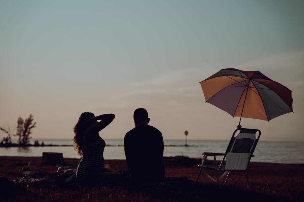 Couple enjoying a peaceful lakeside picnic under an umbrella at sunset.